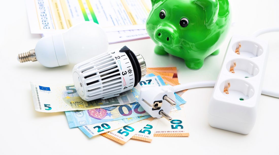 Energiesparen mit Heizthermostat, LED-Lampe, Mehrfachsteckdose und Euroscheinen neben grünem Sparschwein.