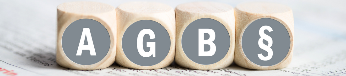 Vier kleine Natur-Holzwürfel, die auf der Frontalansicht jeweils mit einem Buchstaben: A, G, B  und einem Paragraf-Zeichen zusehen ist. 