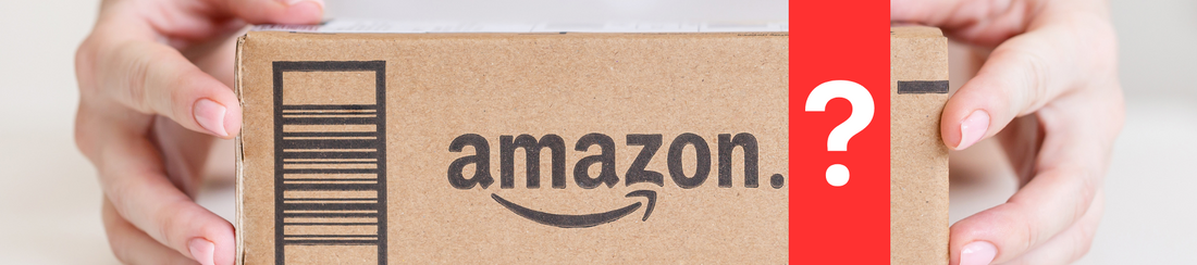 Frontal auf einem Tisch ein Paket zu sehen, wo ein Schriftzug mit Logo von Amazon zu sehen ist. Das Paket wird umringt von beiden Armen einer Person (die Person selbst ist nicht zu sehen).  