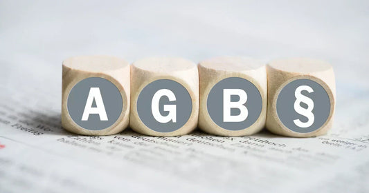 AGB Gesetzestexte rechtssicher im Online-Shop: Vier Holzsteine mit Paragrafen-Symbol auf einem Gesetzestext.