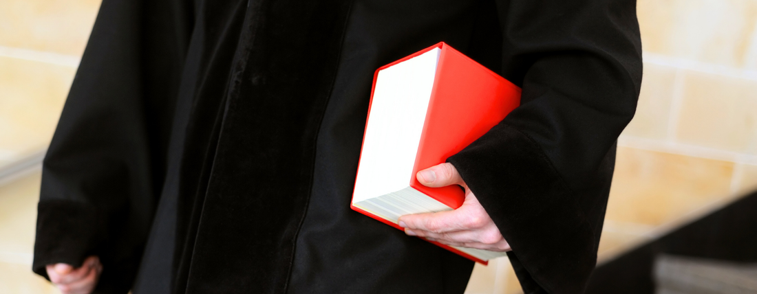 Ein Jurist in einem Anzug läuft eine Treppe hinunter und hält ein rotes BGB-Gesetzbuch (Bürgerliches Gesetzbuch) in der Hand. Symbolbild für Rechtsberatung im Online-Handel.