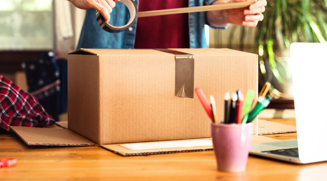 Person verpackt Karton mit Klebeband auf Schreibtisch – Umzug, Versand, Organisation.