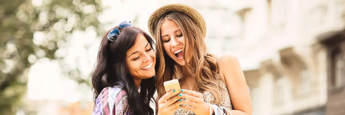 Zwei Frauen nutzen glücklich den Widerrufsbutton am Smartphone für eine rechtssichere Retoure im Online-Handel.