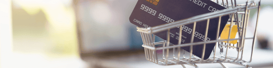 Im Hintergrund ein aufgeklebter Laptop und im Vordergrund ein kleiner Einkaufswagen mit einer Kreditkarte darin.