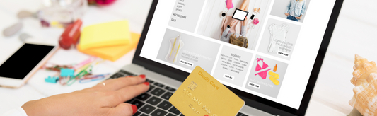 Eine nicht zu sehende Person (nur die Hände) an einem Schreibtisch, an einem geöffneten Laptop beim Online-Shoppen.