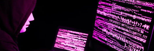 Hacker mit Hoodie vor Monitor voller Code, Symbol für KI Cyberangriff und Online Betrug