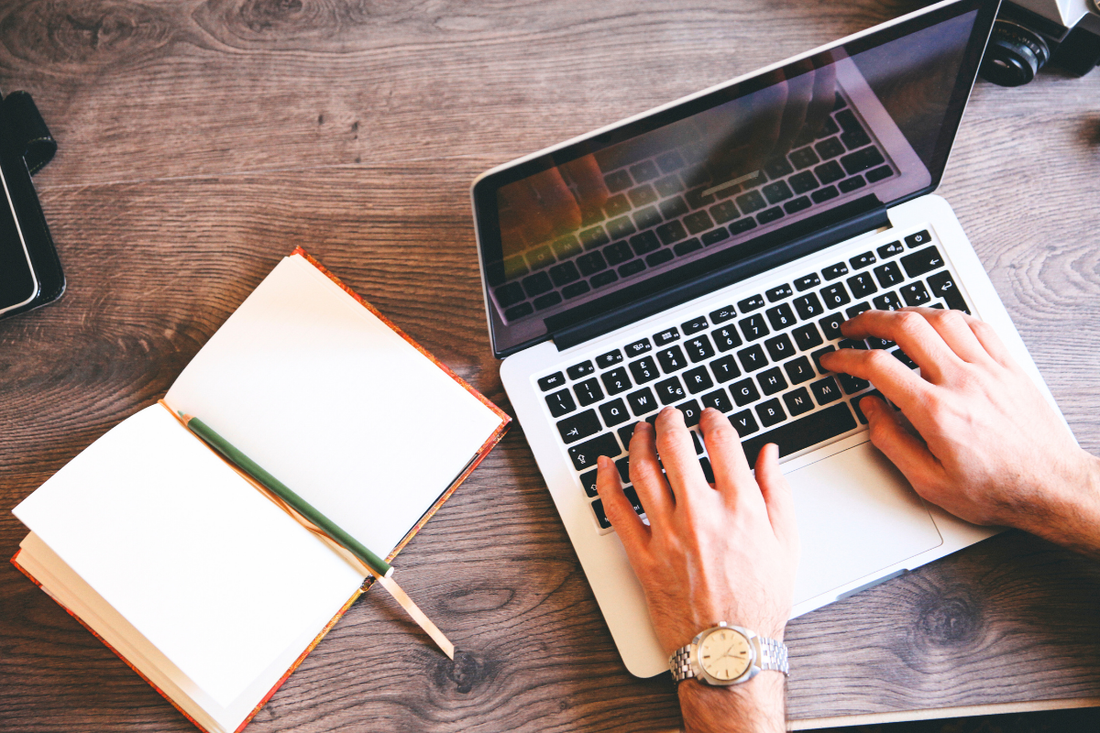 Hände tippen am Laptop neben offenem Notizbuch – effizientes Arbeiten im Homeoffice oder Büro.