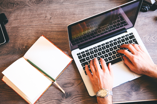 Hände tippen am Laptop neben offenem Notizbuch – effizientes Arbeiten im Homeoffice oder Büro.