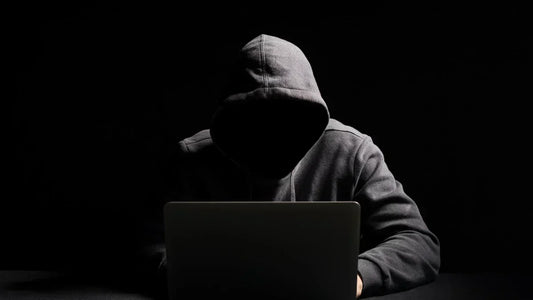 Reverse-Scamming Schutz: Anonymer Hacker mit Kapuze am Laptop – Warnung vor dem Zweitbetrug.