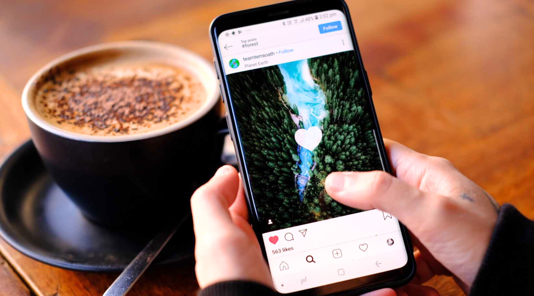 Person nutzt Smartphone mit Instagram am Tisch, daneben Cappuccino – Social Media im Alltag.