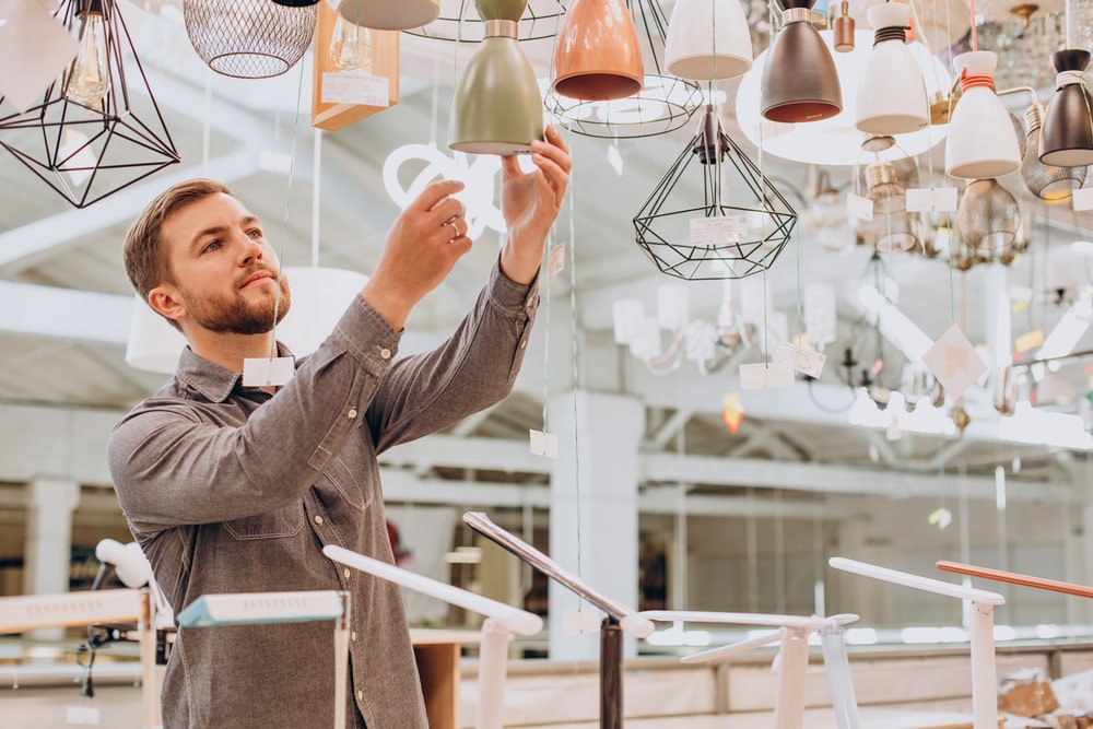 Mann prueft moderne Haengelampen im Fachgeschaeft und waehlt Designleuchten aus Metall und Glas aus.