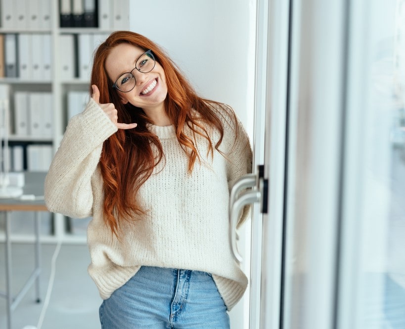 Lachende Frau mit Brille gibt Handzeichen für Anruf – Shopper Safety freundlicher Kundenservice und Kontaktaufnahme.