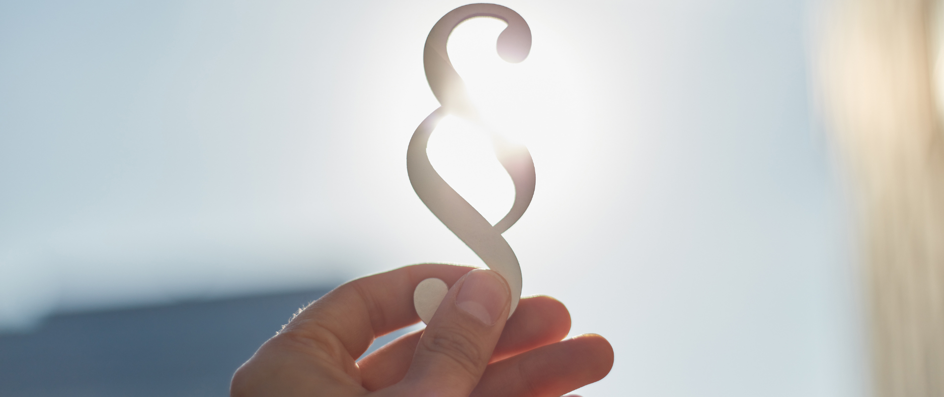 Hand hält Paragraphen-Symbol in die Sonne, Symbolbild für Recht, Gesetz und juristische Themen.