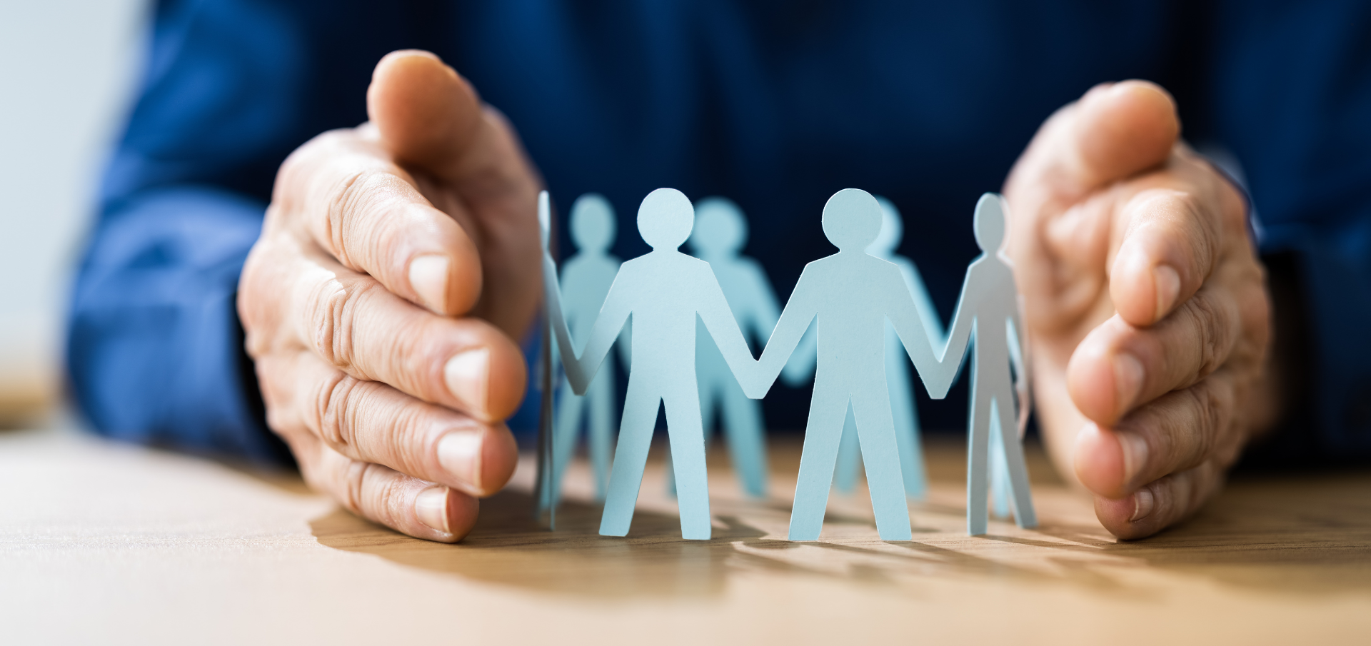 Hände schützen eine Papier-Menschenkette – Symbol für Sicherheit, Schutz und Gemeinschaft. 