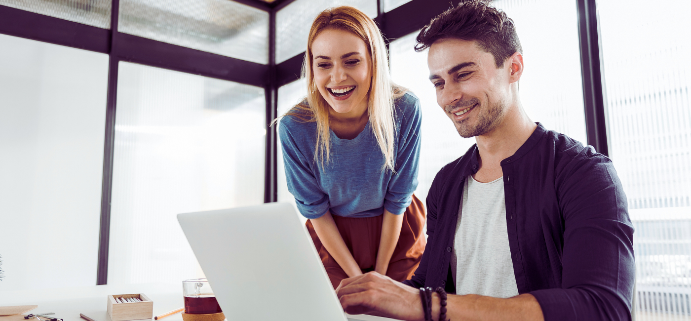 Zwei Kollegen arbeiten lächelnd am Laptop im modernen Büro und entwickeln kreative digitale Projekte.