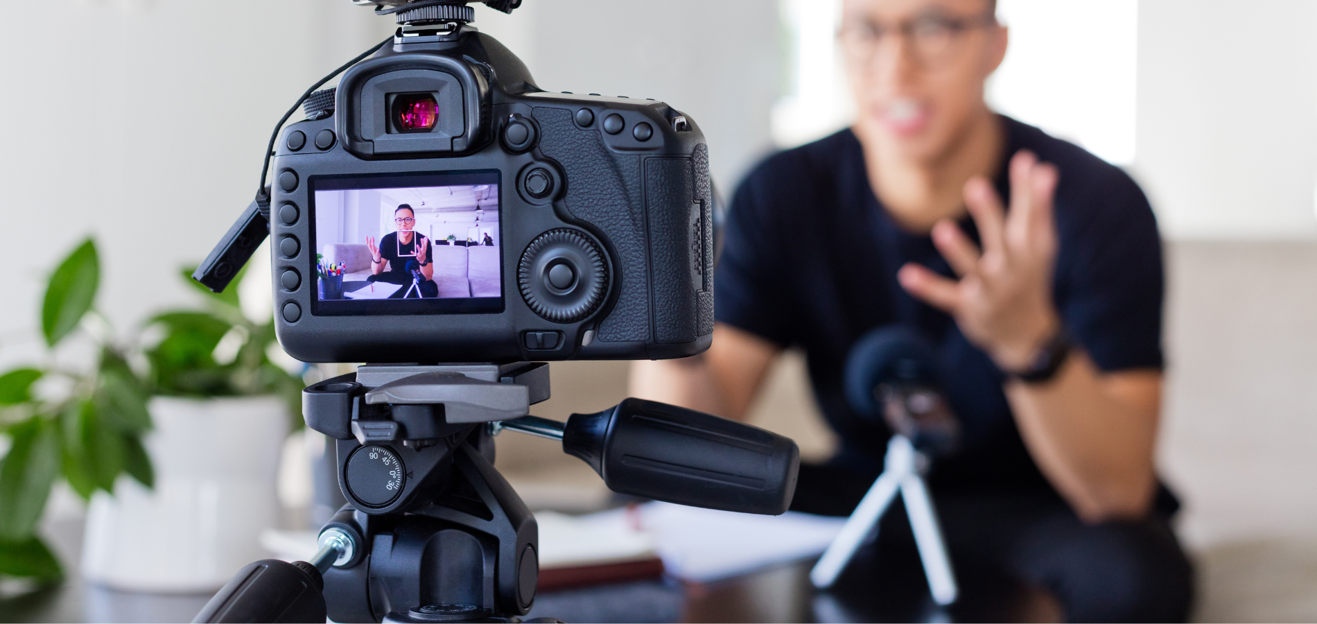 Person nimmt mit einer Kamera ein Video auf, Fokus auf Display und Kamera, im Hintergrund unscharfe Person beim Sprechen.